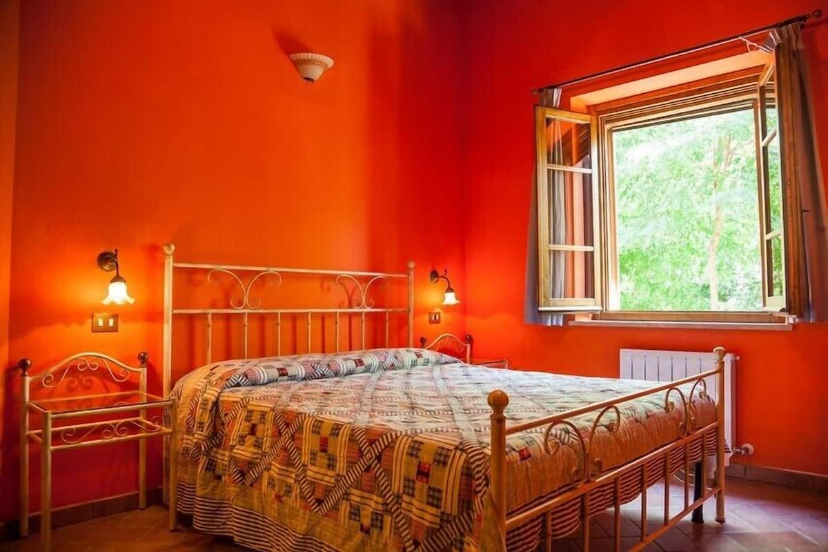 Une chambre à coucher avec un lit, une chaise, une fenêtre avec des rideaux et des lampes fixées au mur.