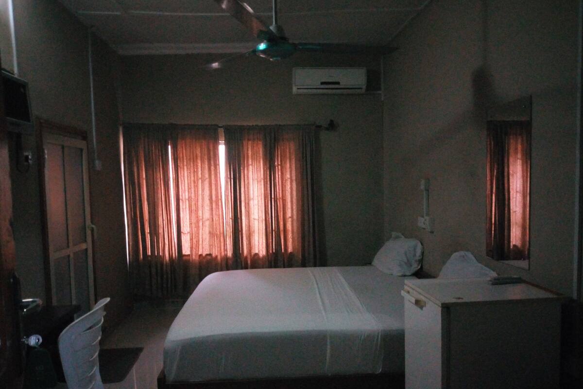 A hotel room with a bed, a chair, a desk, and a ceiling fan.