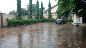 A wet courtyard with a car parked in the middle, surrounded by greenery and a building with a satellite dish. - Abeokuta Hill View Hotel (Abeokuta)