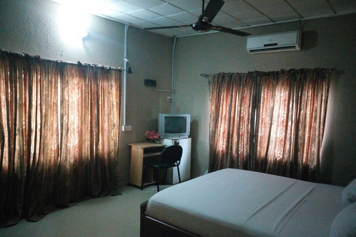 A hotel room with a bed, a desk with a computer, curtains, and a ceiling fan.