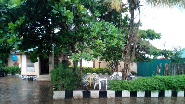 A paved outdoor area with a bench and chairs, surrounded by greenery and a building with a satellite dish. - Abeokuta Hill View Hotel (Abeokuta)