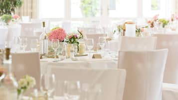 Un salón de banquetes con mesas redondas dispuestas para un evento formal, con manteles blancos, cristalería y centros de mesa florales.