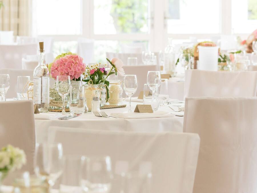 Un salón de banquetes con mesas redondas dispuestas para un evento formal, con manteles blancos, cristalería y centros de mesa florales.
