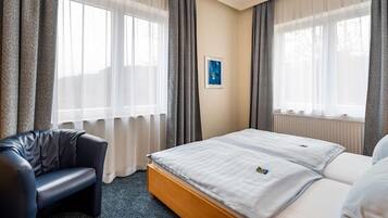 A hotel room with a bed, a chair, and large windows with curtains.
