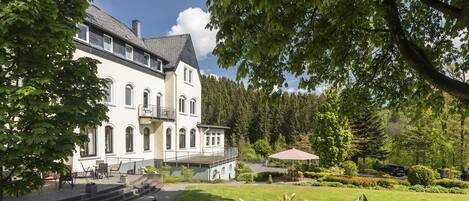Ein großes, mehrgeschossiges Gebäude mit einer symmetrischen Fassade, einer zentralen Treppe und einem gepflegten Garten mit einer Terrassenfläche.