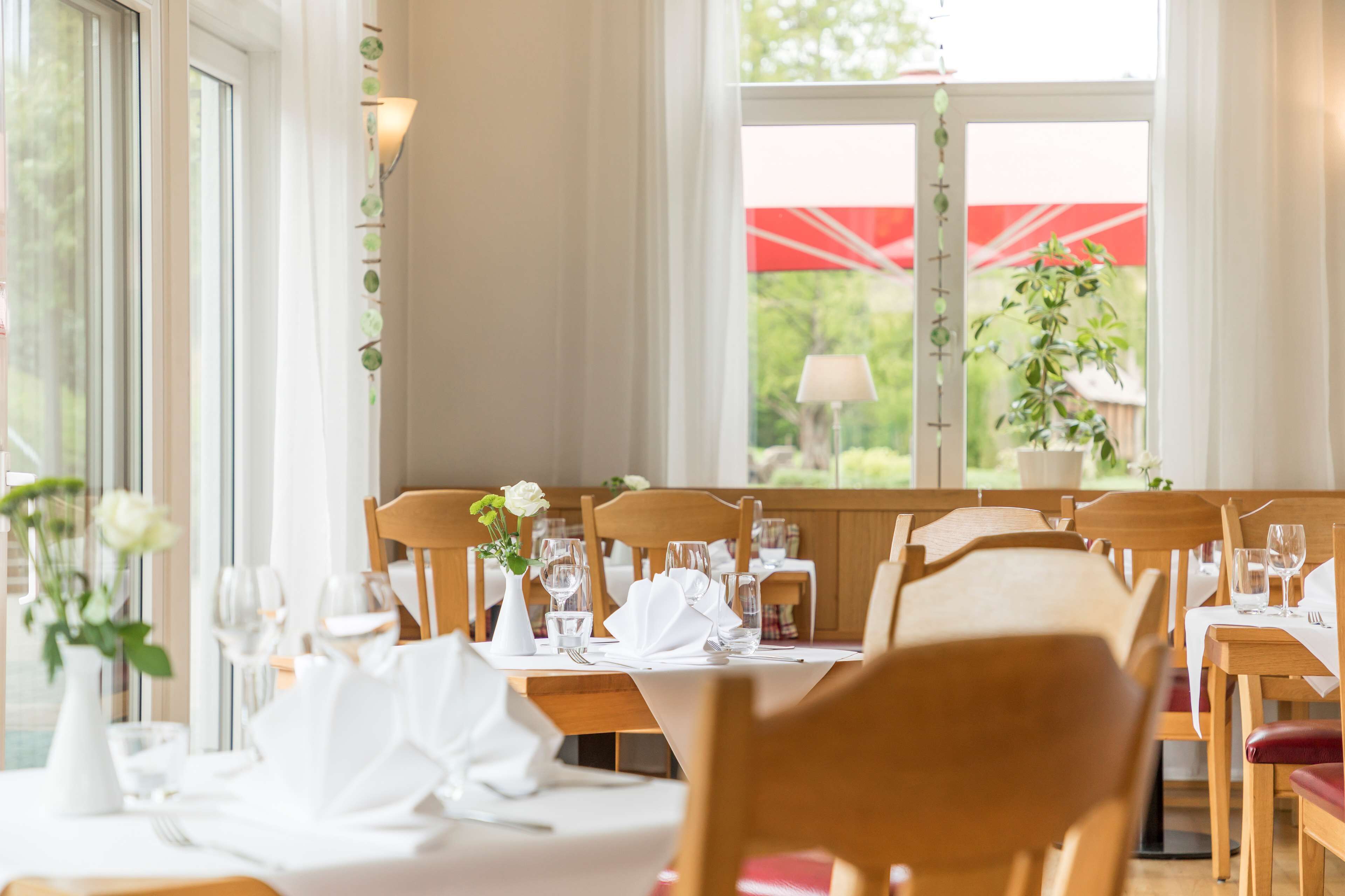 Un ristorante con tavoli e sedie in legno, tovaglie bianche e bicchieri.