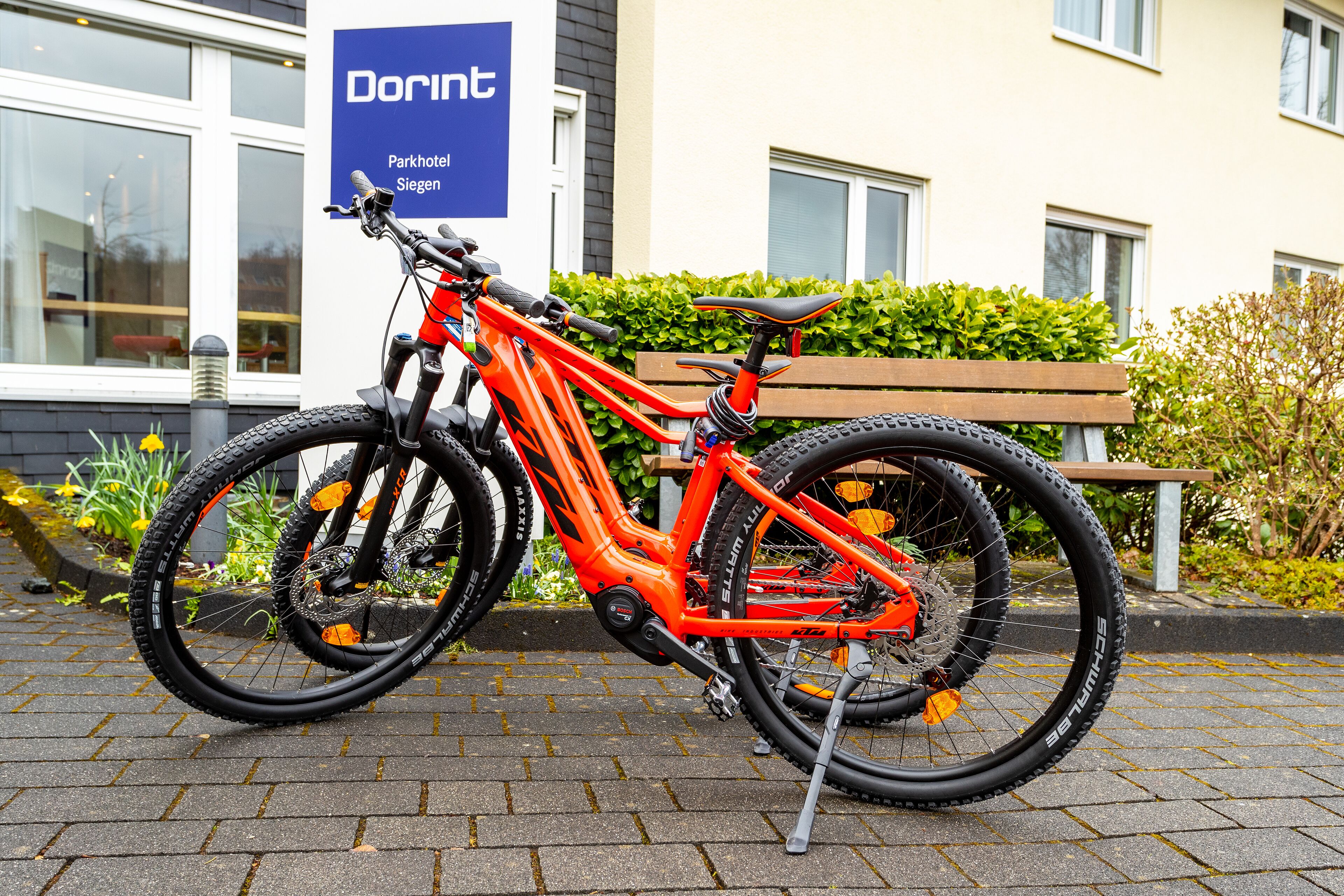 A red mountain bike parked in front of a building with a sign that reads "Dorint Parkhotel Siegen".