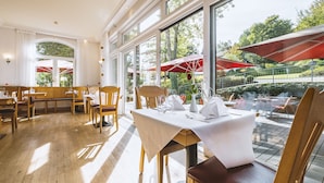 A restaurant with wooden tables and chairs, large windows, and outdoor umbrellas. - Dorint Parkhotel Siegen (Siegen)