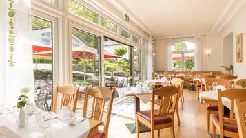 Een restaurant met grote ramen, houten tafels en stoelen.