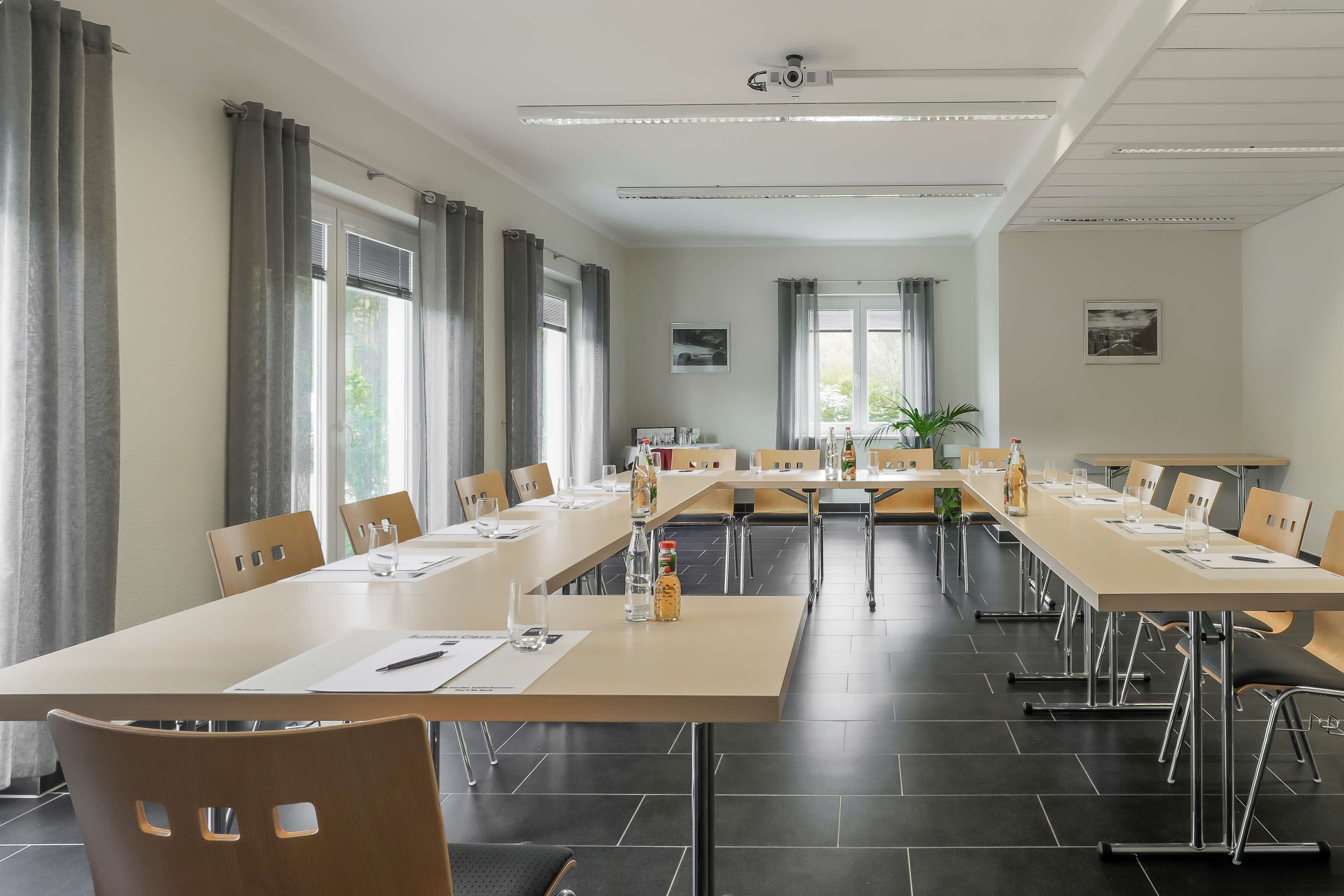 A conference room with long tables, chairs, and a ceiling-mounted projector.