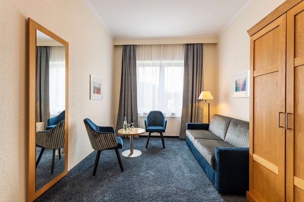 Une chambre d’hôtel avec un grand miroir, une table ronde avec des chaises, un canapé, une lampe et une armoire.