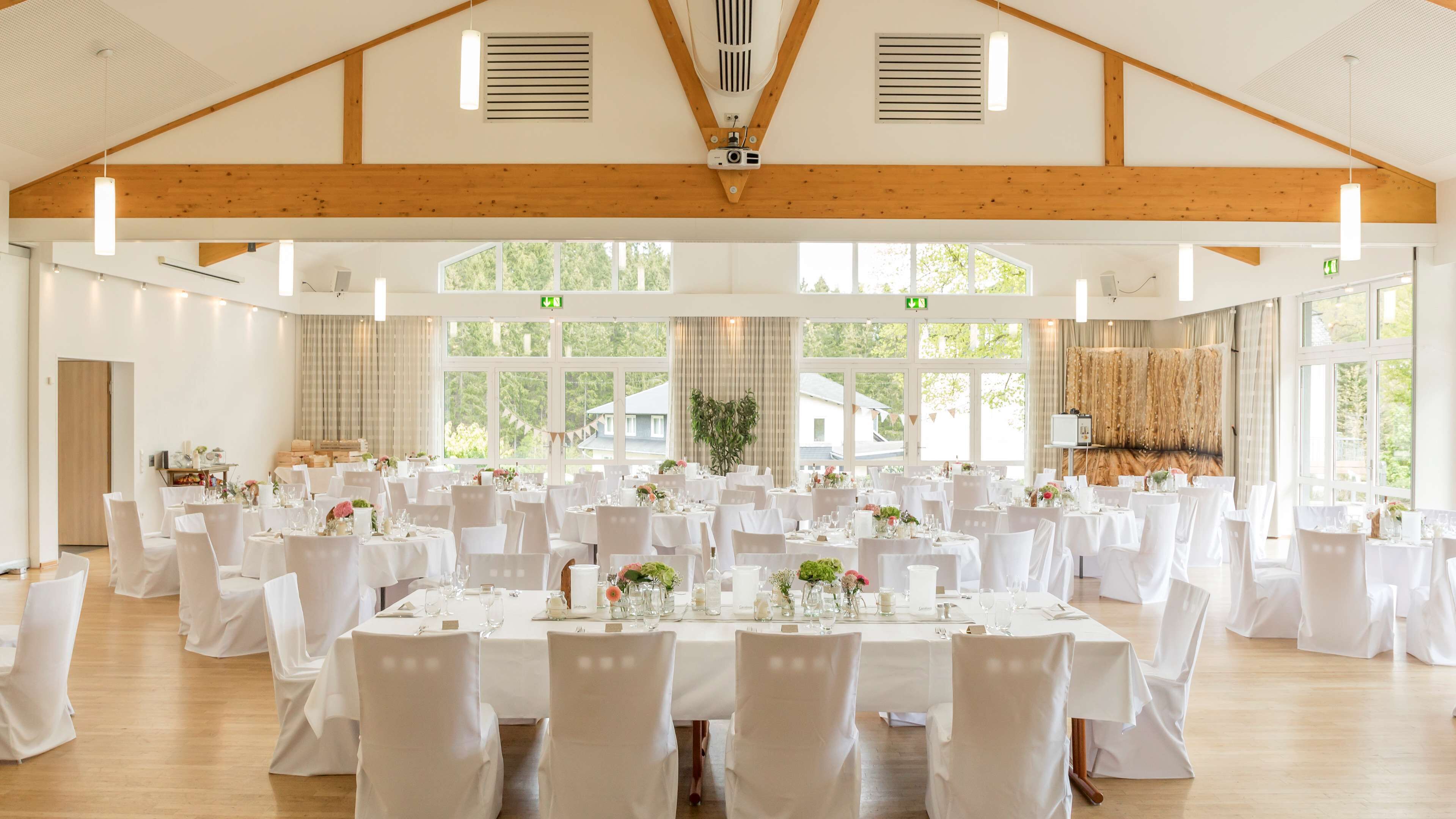 Un amplio salón de banquetes con techos altos y vigas de madera, con varias mesas redondas dispuestas para una cena.