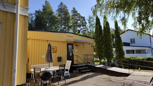 A yellow building with a covered outdoor seating area, a barbecue grill, and a staircase leading to a door. - Rosenlund - Hostel (Fagersta)