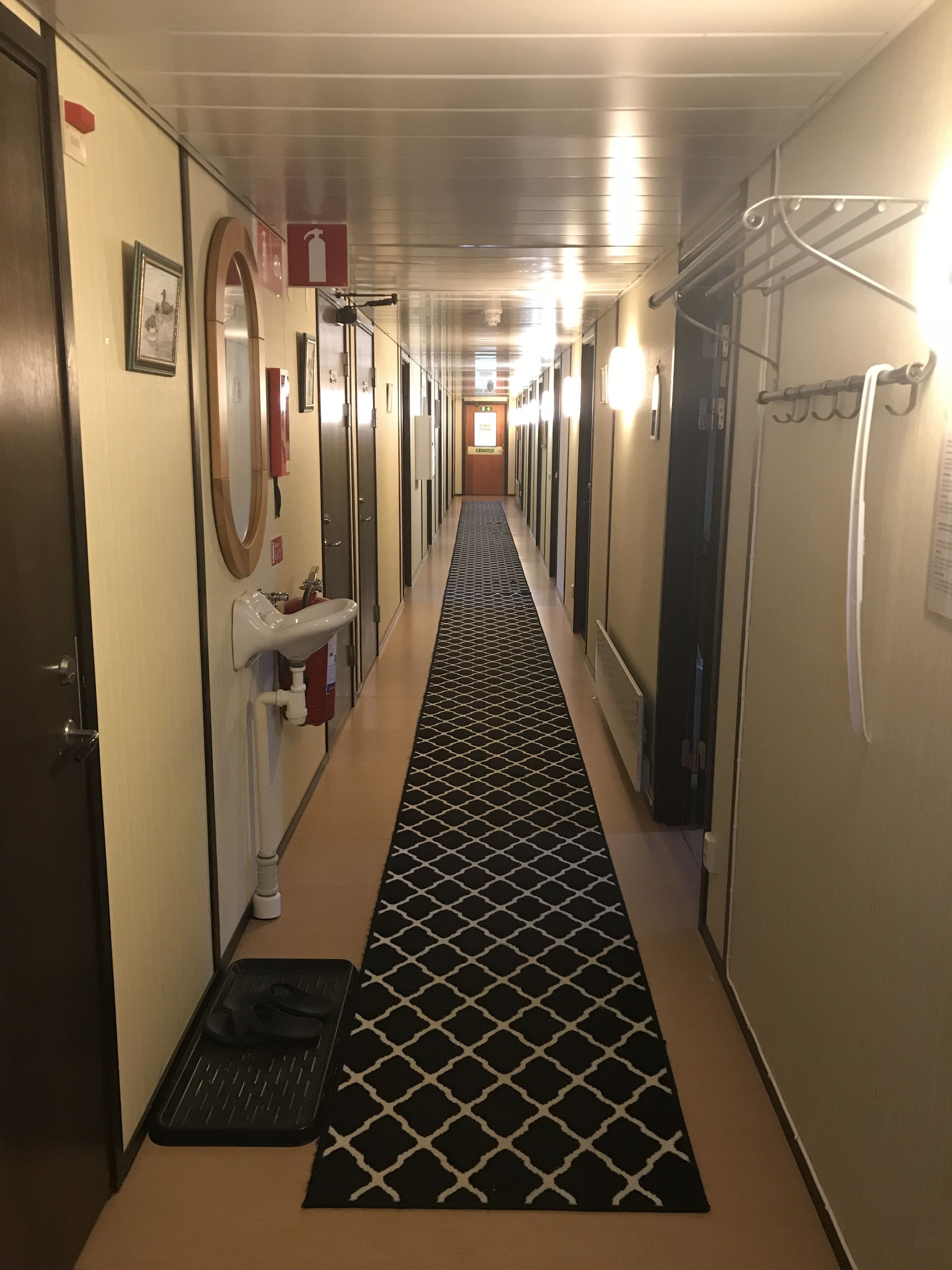 Pasillo de hotel con alfombra de diseño blanco y negro, un lavamanos y un espejo en la pared izquierda.