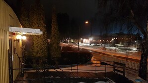 A nighttime view of a street with snow on the ground, a building with a lighted sign, and a fence in the foreground. - Rosenlund - Hostel (Fagersta)