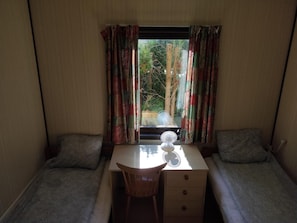 A small room with two single beds, a desk with a chair, and a window with curtains.