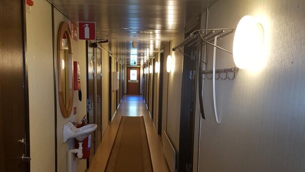 A long, narrow hotel corridor with doors on both sides, a central walkway, and overhead lighting. - Rosenlund - Hostel (Fagersta)