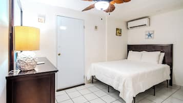A bedroom with a bed, a ceiling fan, a wall-mounted air conditioner, and a door.