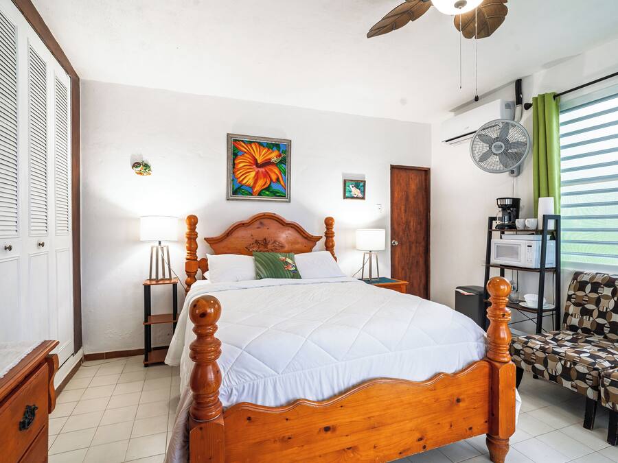 Un dormitorio ordenado con cama de madera, mesitas de noche, una silla y un ventilador.