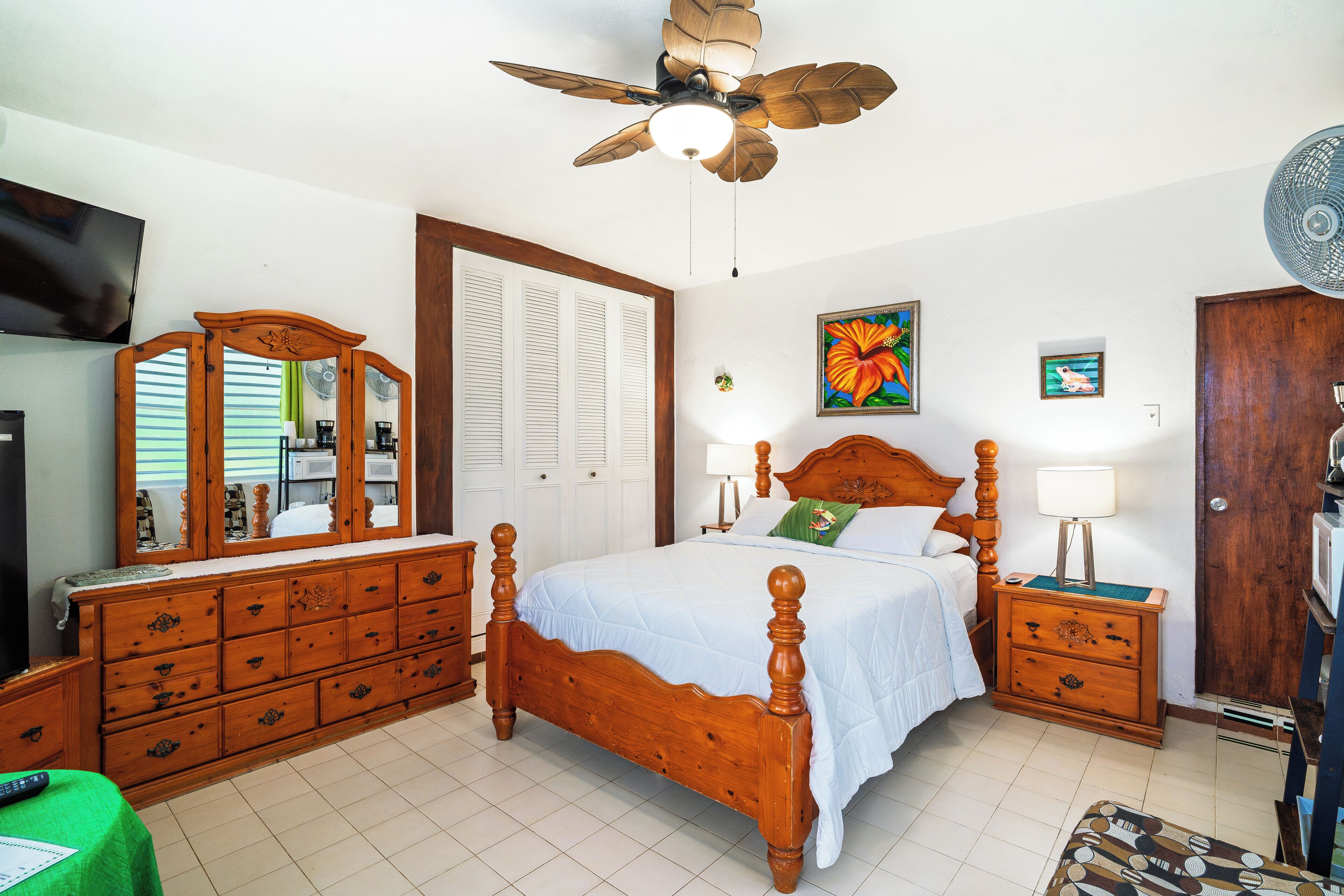 A bedroom with a wooden bed, a ceiling fan, a dresser, a TV, and a door.