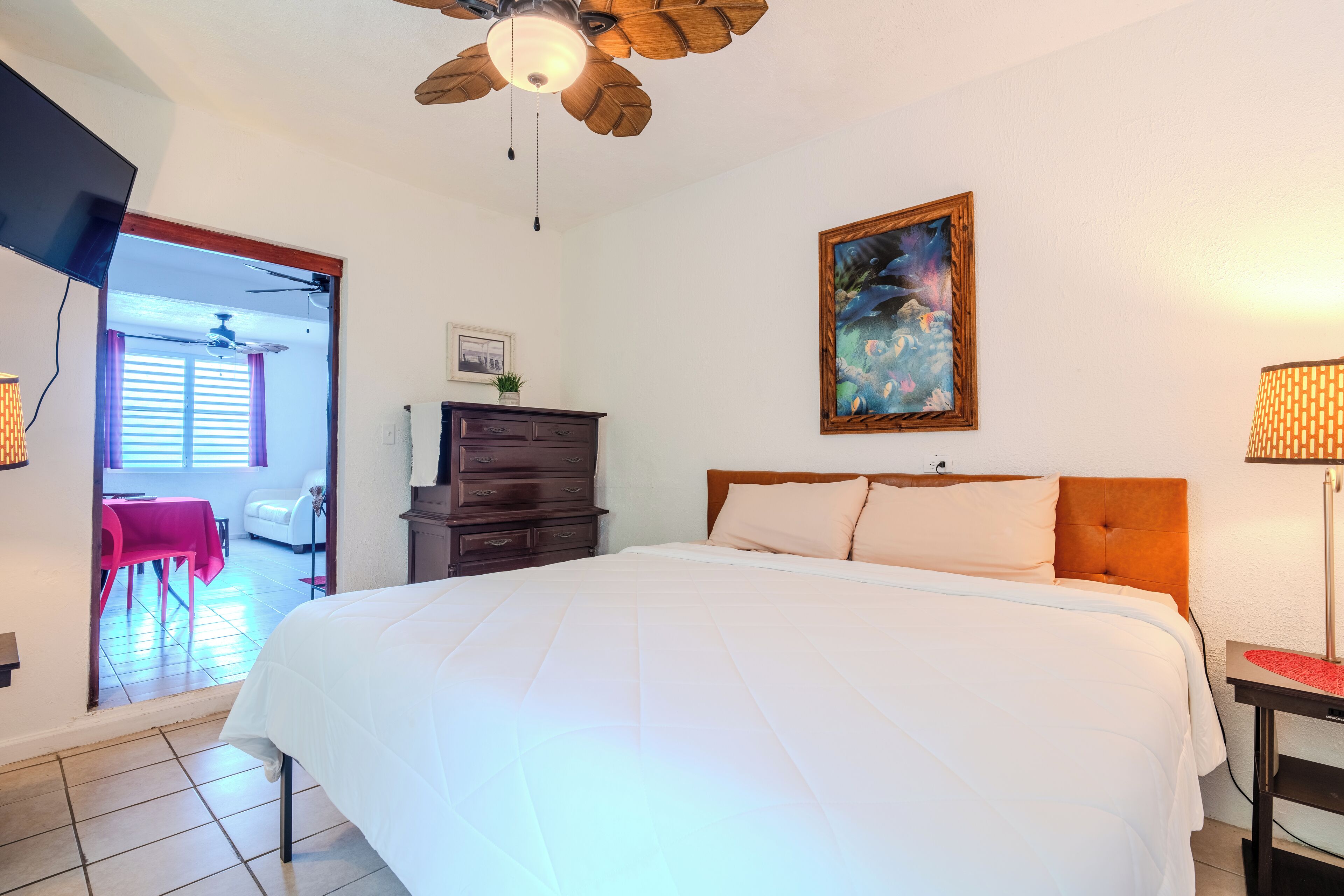 Ein Schlafzimmer mit einem großen Bett, einem Deckenventilator, einem Gemälde, einem Schminktisch und einem Schreibtisch mit Lampe.