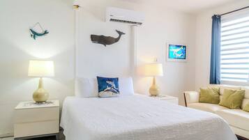 A hotel room with a bed, two bedside tables with lamps, a sofa, an air conditioning unit, and wall art.