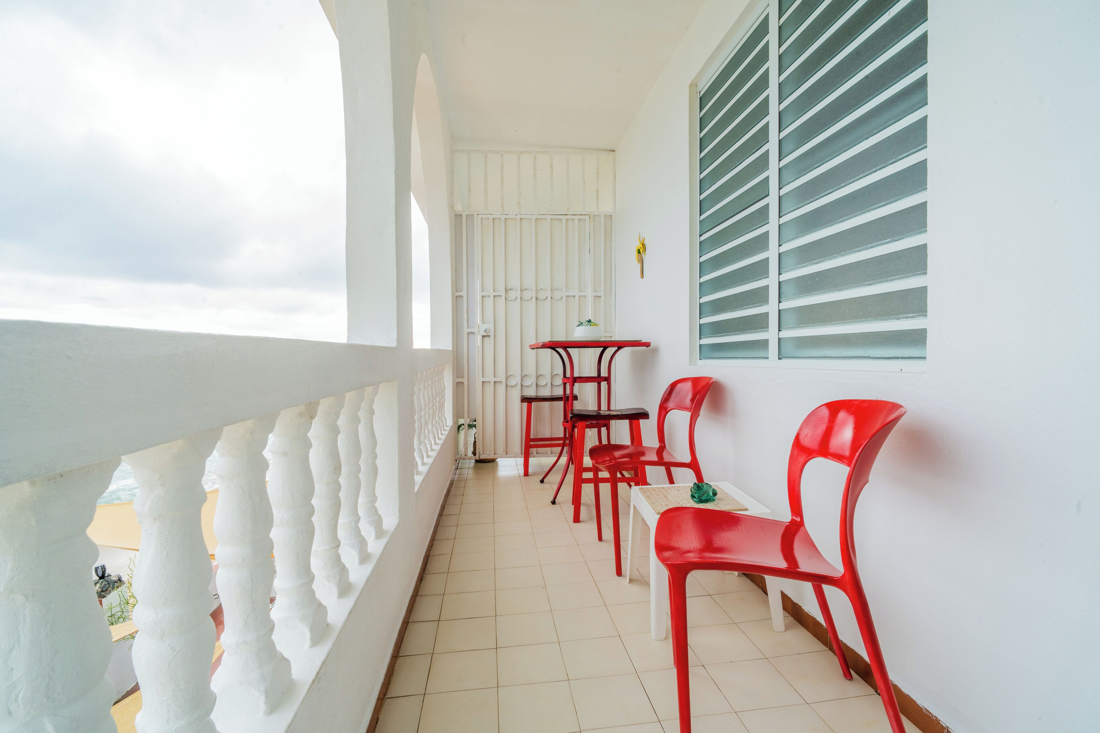 A balcony with a white railing, a table with chairs, and a window with blinds.