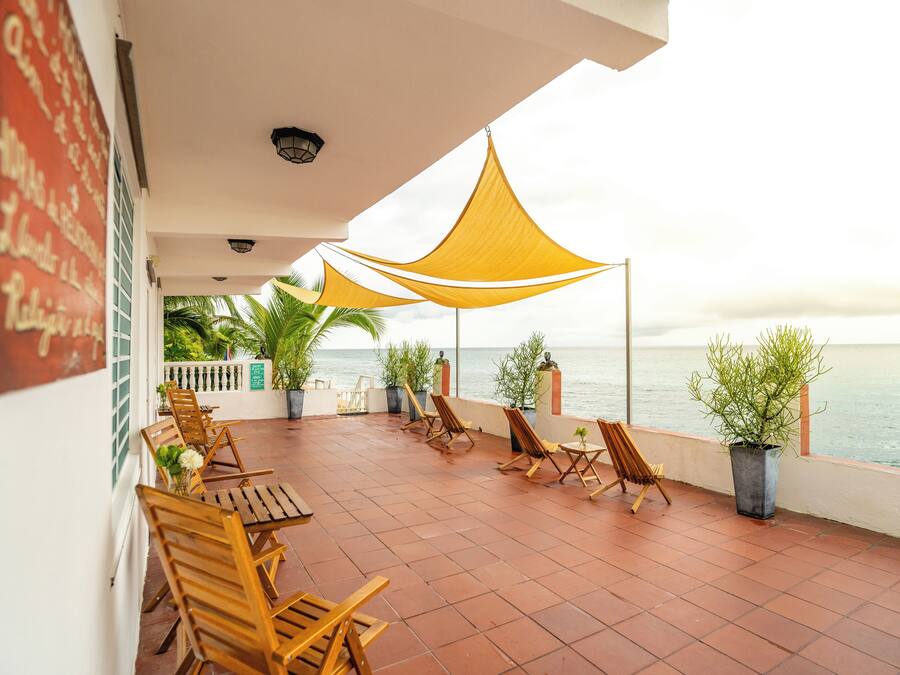 Eine Terrasse mit Holzhöckern und -tischen, gelben Sonnenschirmen, Topfpflanzen und Blick auf das Meer.