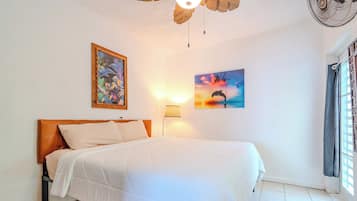 A neatly made bed with a wooden headboard, a wall-mounted lamp, and two framed artworks.