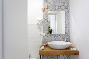 A bathroom with a large white sink, a wooden vanity, a mirror, and patterned tiles on the walls. - Reusuite Authentic Sicilian Hospitality (Ragusa)