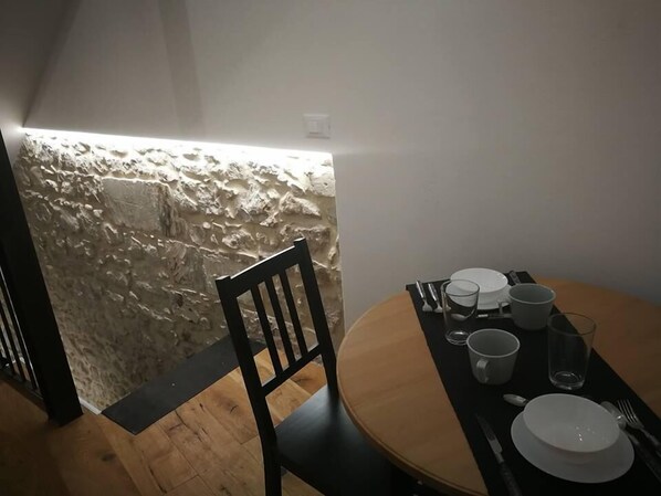 A dining area with a round table set for two, a chair, and a stone wall in the background. - Reusuite Authentic Sicilian Hospitality (Ragusa)
