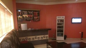 Uma área de bar com prateleiras de garrafas, uma geladeira com a etiqueta 'RESTP INT' e uma tela de televisão.