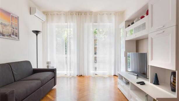 Una sala de estar moderna con un sofá, televisor y muebles blancos.