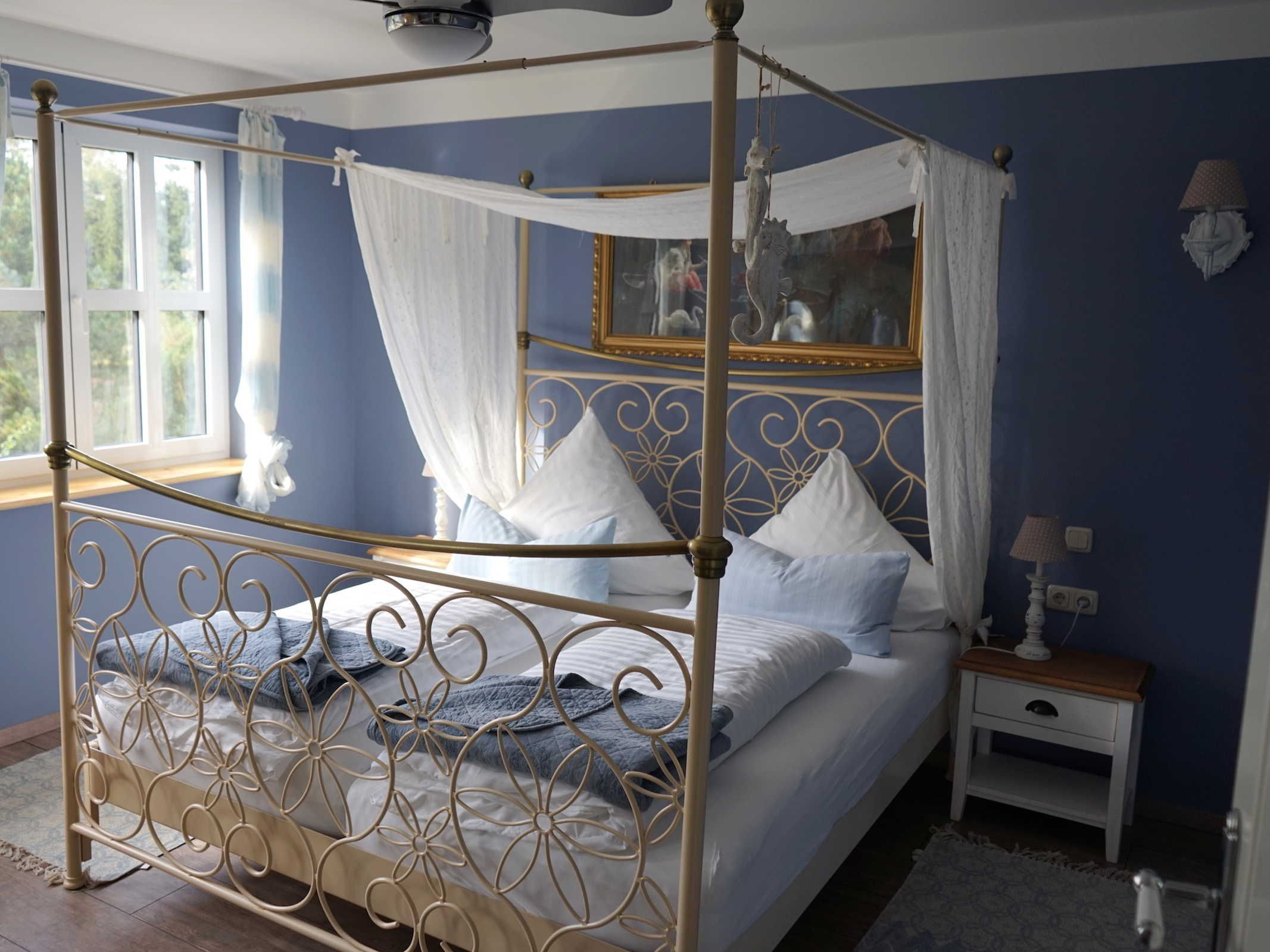 Ein Himmelbett mit Baldachin, ein Nachttisch mit Lampe und ein Spiegel an der Wand.