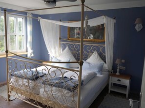Een hemelbed met hemel, een nachtkastje met lamp en een spiegel aan de muur.