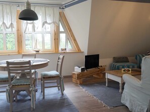 Et hyggeligt rum med spisebord, stole, fjernsyn og en seng med stribet sengetøj.
