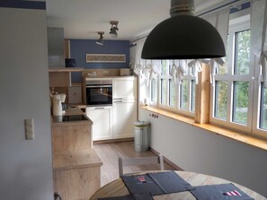 Et lille køkken med hvide skabe, en indbygget ovn og et vindue med gardiner.