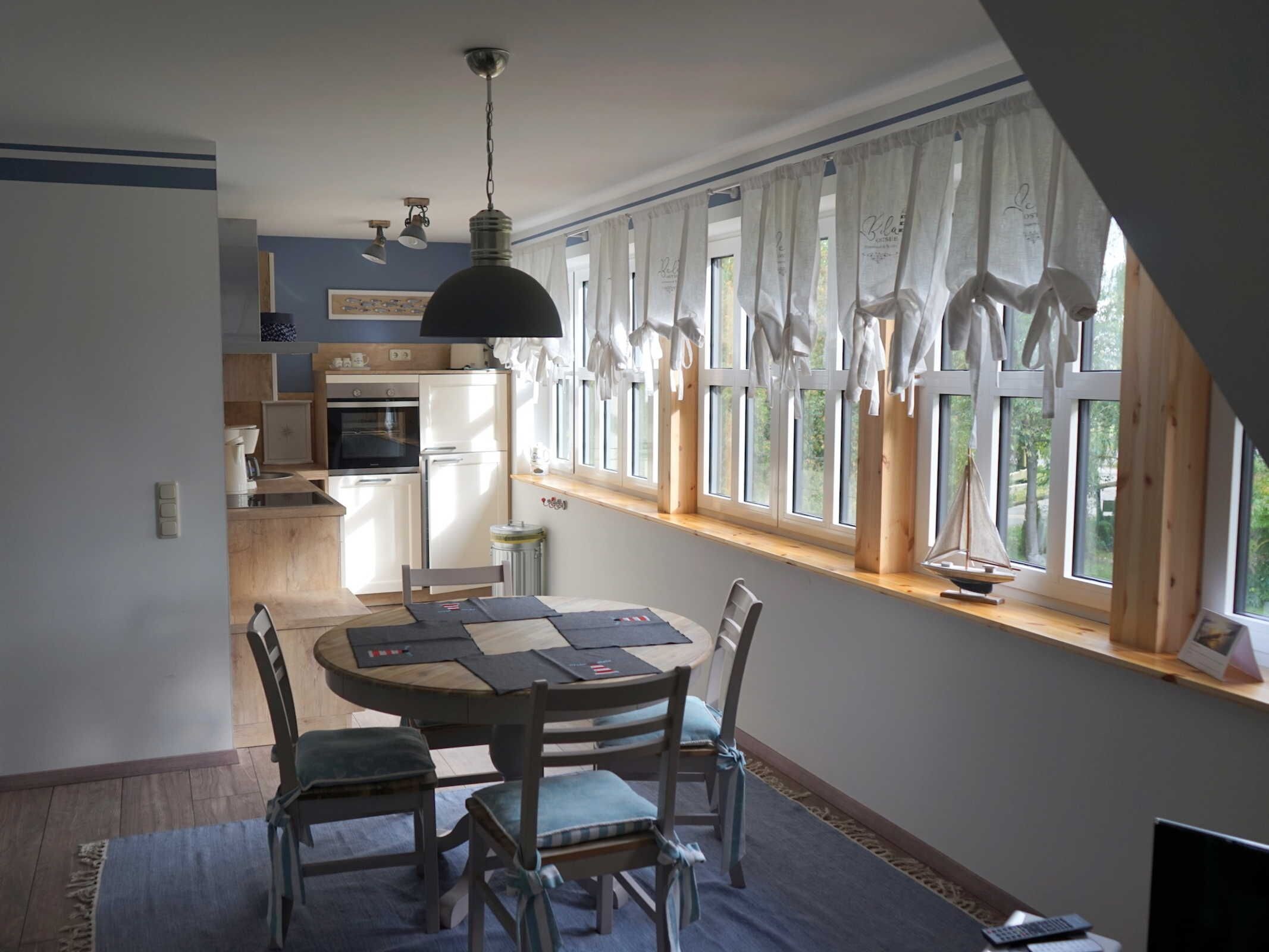 Un coin repas comprenant une table ronde, quatre chaises et une vue sur la cuisine grâce à de grandes fenêtres.