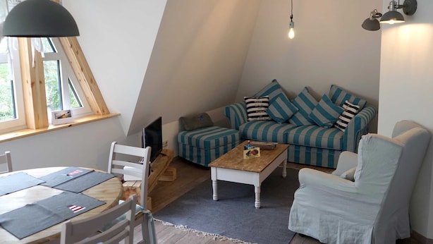 Un salon chaleureux de style loft, doté d’un plafond en pente, d’un canapé à rayures, d’un fauteuil blanc, d’une table basse en bois et d’une table à manger avec des chaises.