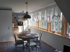 Een eetgedeelte met een ronde tafel, vier stoelen en uitzicht op de keuken door grote ramen.