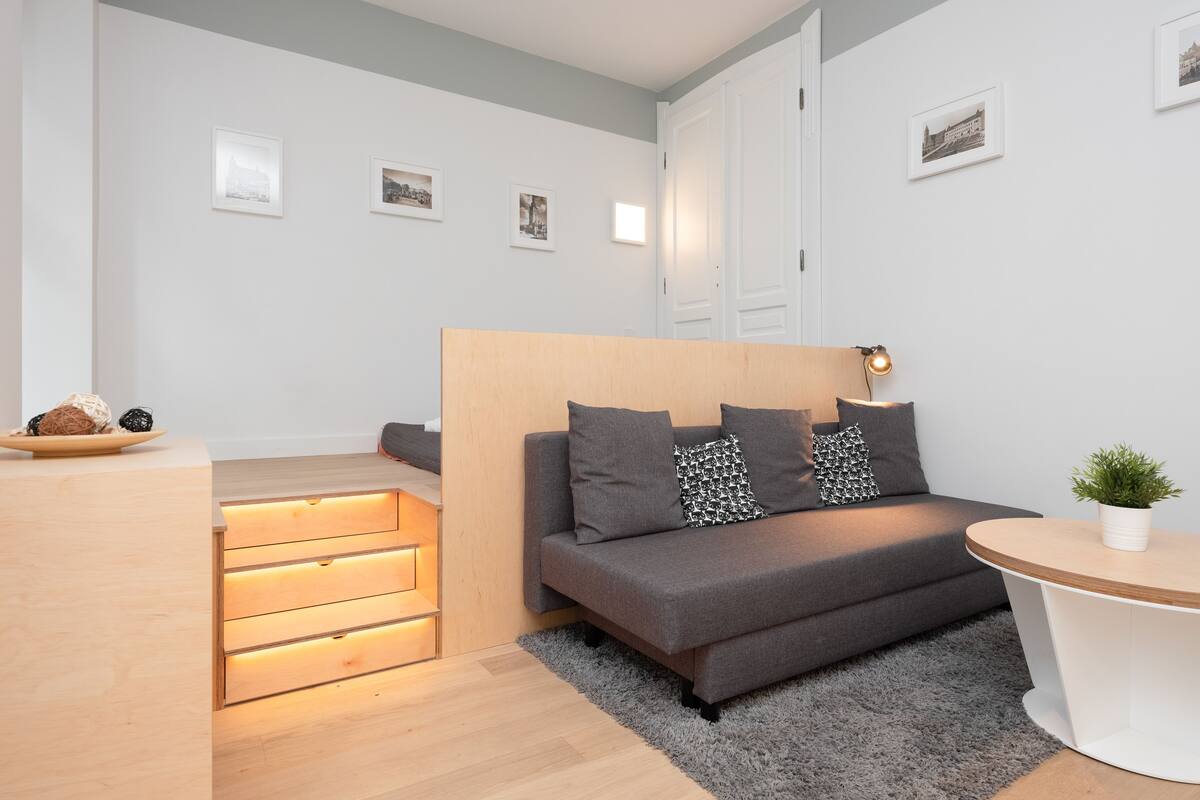 A modern bedroom with a bed, bedside tables, a small desk, and a plant.