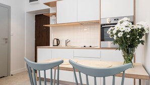 Une cuisine moderne avec des armoires blanches, un comptoir en bois et un four encastré. On y trouve deux chaises bleues et un vase avec des fleurs blanches sur la table.