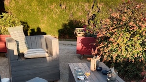An outdoor seating area with a wooden bench and a table, surrounded by gravel and greenery. - La Grange 41 (Vouzon)
