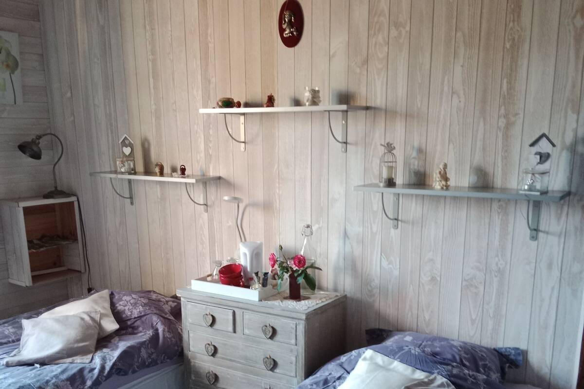 A bedroom with two beds, wooden panel walls, and shelves with decorative items.