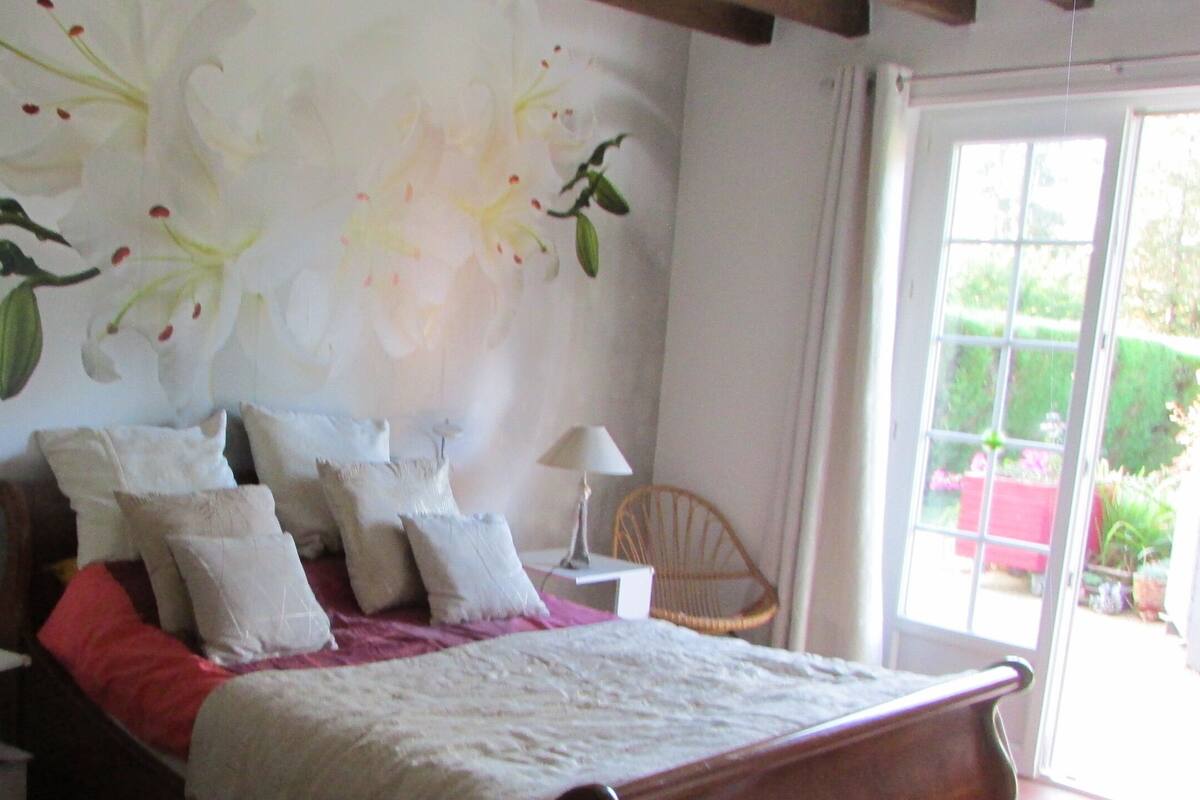 A bedroom with a bed, pillows, a nightstand, a lamp, and a chair.