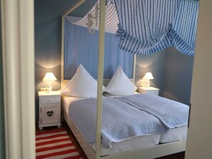 Un lit à baldaquin avec des draps blancs, deux tables de chevet avec des lampes et un ciel de lit à rayures.