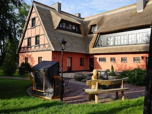 Ein traditionelles Gebäude mit einem Reetdach, einer hölzernen Bank und einem kleinen Garten.