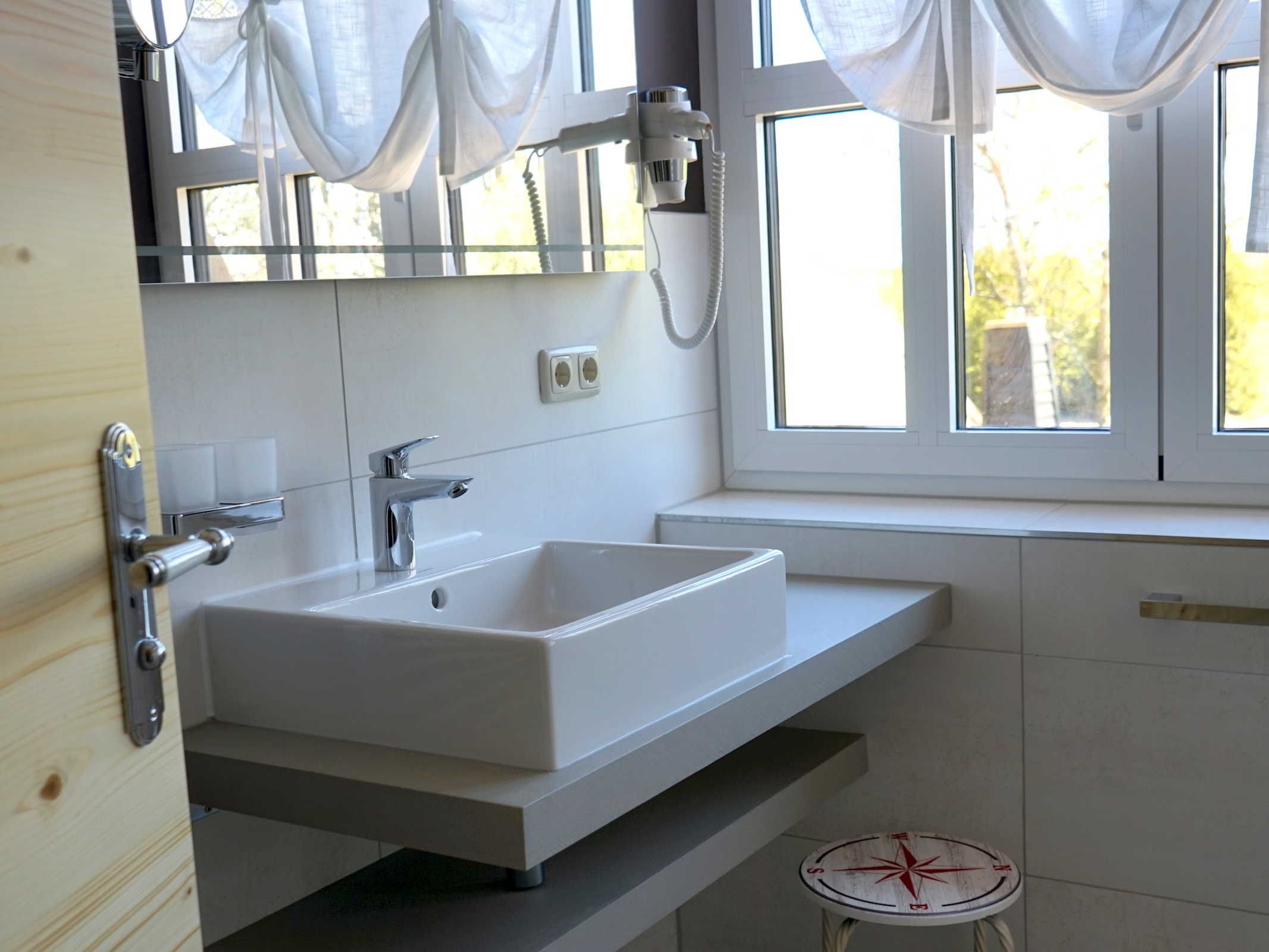 Un baño moderno con un lavamanos blanco, un espejo y una ventana con cortinas.