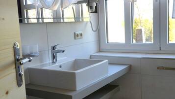 Un baño moderno con un lavamanos blanco, un espejo y una ventana con cortinas.