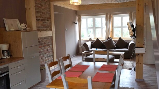 Un espacio de sala cómodo con un sofá, una mesa de comedor con sillas, una cocina con refrigerador y una pared de ladrillo.